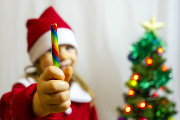 Christmas caramel in the hand of a girl in a santa claus suit against a blurred background