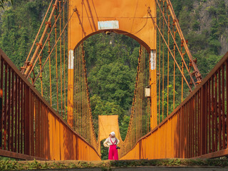 Female tourists stand to see the view on the orange iron suspension bridge, a popular tourist spot in Vangvieng city. Vientiane, Laos