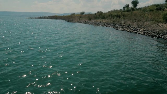 Low aerial of rocky shoreline of calm lake, sea of galilee, Israel. Wide shot
