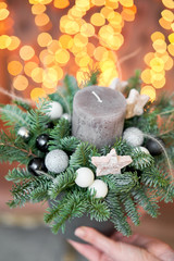 Small arrangement of fresh spruce with a candle in a ceramic pot. Christmas mood. Bokeh of Garland lights on background.