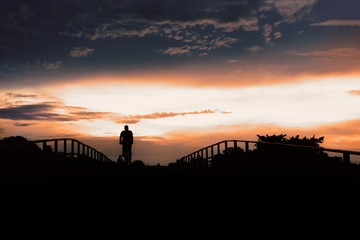 Fototapeta na wymiar Silhouette of active people on pedestrian bridge against low sunset