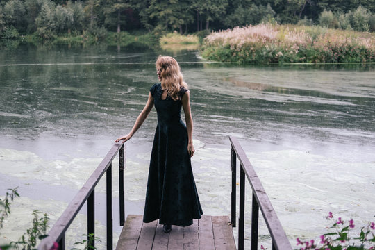 Portrait of fashion female wearing Hollywood wave hair style and long dress, standing on the bridge near beautiful dirty pond