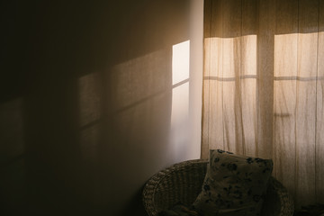 cozy window with curtains in the room. Shadow and sunlight on the wall. Pillow in wicker chair