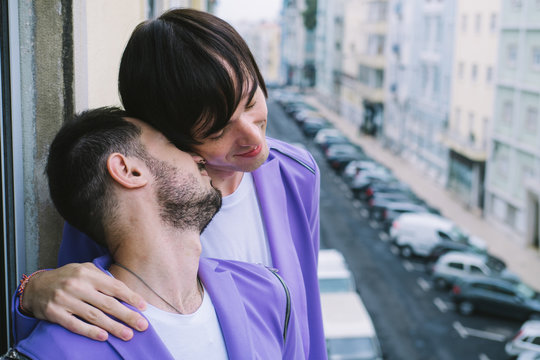 Happy gay couple standing on the balcony together. European street view on background