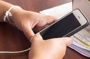 The phone in the hands of an Asian woman is holding and pressing a button while plugging in a...