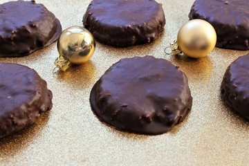 Six chocolate covered homemade Elisenlebkuchen a german christmas cookie specialty. Nicely decorated with golden christmas tree balls on a golden glitter background