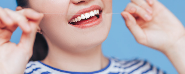 Happy smiling woman with white perfect teeth flossing, dental floss on blue background, clode up...