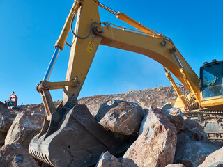 Excavator is moving a rock boulders during road construction on the rocky soils