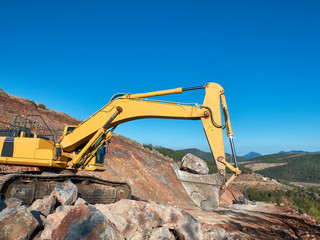 Excavator is moving a rock boulders during road construction on the rocky soils