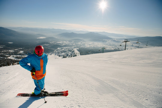 Skier wearing helmet standing on snow mountain top, sunny day, beautiful view