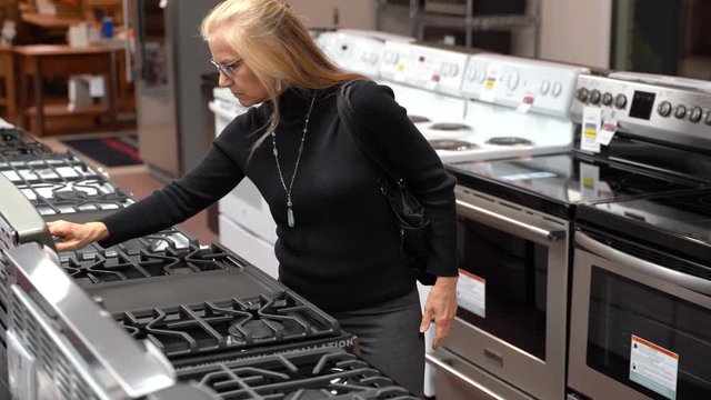 Closeup of pretty mature blonde woman looking at the features and benefits of a gas stove in a kitchen appliance store.