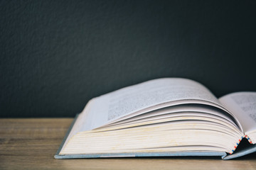 An old book open on wooden table with black color wall background and light frome above, copy space