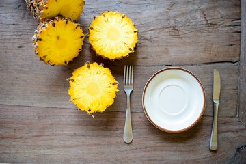 Ripe pineapple slice is served with plate, knife and fork on the wooden table.