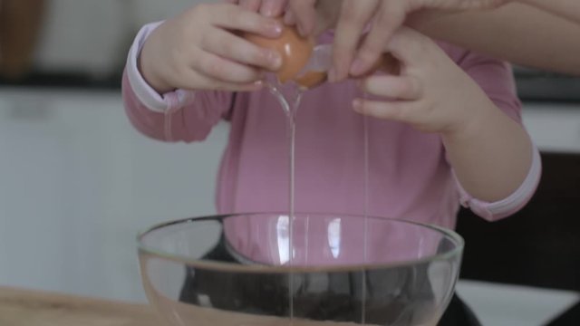 little girl breaks eggs in a bowl for making cookie dough