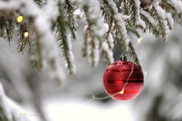 Christmas and New Year winter festive background.Red Christmas ball and shining garland on a spruce  branch on a blurred winter snow forest background.IPhone Wallpaper. Winter festive decor