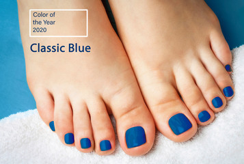 The trend color of the year 2020 Classic Blue. Female legs with pedicure on a white towel close up, top view