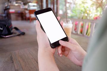 Mockup picture of human’s hands holding smart phone with white blank screen in modern place.