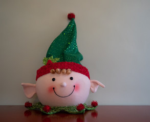 Close Up of a Smiling Christmas Elf Decoration on a Red Table