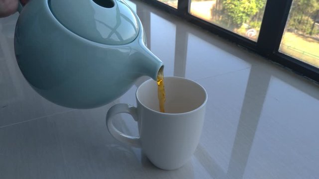 Tea being poured from a teapot into an empty white mug.