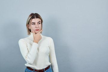 Portrait of young woman in pastel pink shirt thinking gesture, looking aside, keeping hand on chin...