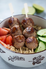 Fototapeta na wymiar Closeup of meatball skewers, quinoa and fresh vegetables, vertical shot, selective focus