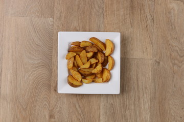 Potato wedges in a white square plate on wooden background