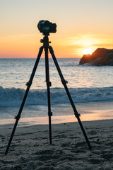 Camera standing on a tripod on the beach against the background of dawn