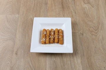 fried mozzarella sticks crispy on a white plate isolated on wooden background - top view