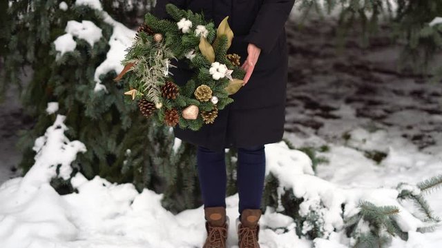 Legs in boots of the girl with christmas wreath in hands. Snowy winter day