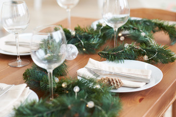 Christmas table setting with plates, silverware, gift box and decorations green branches and cones. on a wooden table