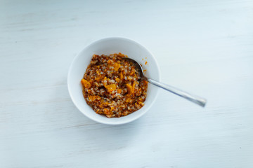 buckwheat, cooked with pumpkin, in a white Cup on a light background, shot by the light from the window