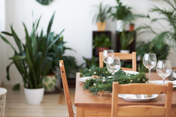 Christmas table setting with plates, silverware, gift box and decorations green branches and cones. on a wooden table