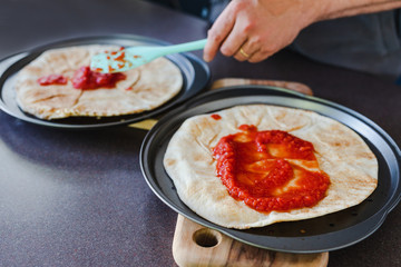 pizza bases with tomato sauce being spread on them