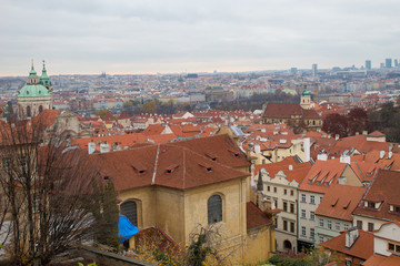 Fototapeta premium Panorama of the Czech city of Prague with tiled orange roofs from the observation deck of Prague Castle on a cloudy day on the eve of Christmas.