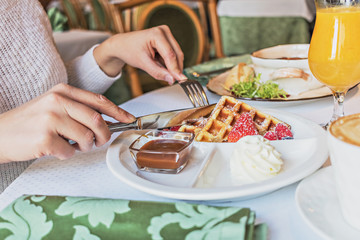 Delicate waffles with fresh strawberries and cream for breakfast. Hands of a girl with cutlery at the table.Black and white photo.