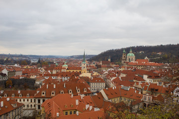 Obraz premium Panorama of the Czech city of Prague with tiled orange roofs from the observation deck of Prague Castle on a cloudy day on the eve of Christmas.