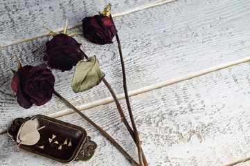 Three Burgundy, dried roses, and a decorative tray with leaves in the shape of hearts, created by nature, lie on a textured white surface. Horizontal layout, copy space.