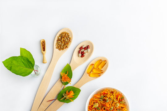 Herbal capsule, natural vitamins, dry calendula flowers at wooden spoon on white background. Concept of healthcare and alternative medicine: homeopathy and naturopathy.