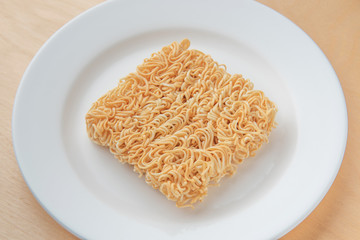 Instant noodles on white disk, wood background, top view