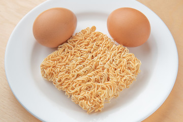 Instant noodles and eggs on white disk, wood background, top view
