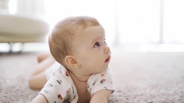 Attractive Caucasian baby girl with crossed eyes lying down alone on the carpet in the living room at home. Shot in 4k resolution