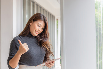 Young business woman in smart casual wear standing outside the office looking at tablet and hand thumb up