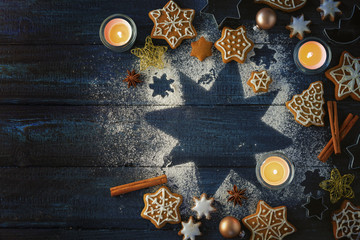 Gingerbread cookies, spices and burning candles on a star from icing sugar on a dark blue wooden background as a Christmas flat lay with copy space, high angle view from above