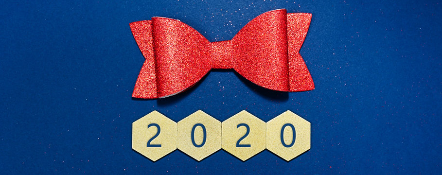 2020 written on gold wooden hexagons  with red christmas bow in a conceptual image of the coming new year. Over blue background.