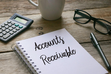 Pen,glasses, a cup, calculator and notebook written with Accounts Receivable on wooden background.