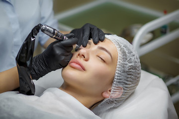 Permanent make up eyeliner procedure, applying on young girl. Close-up. Young beautiful woman...
