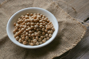 Soybeans in a white plate on rug sack on wooden background. 
