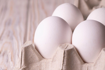 White chicken eggs in a stand. White wood background