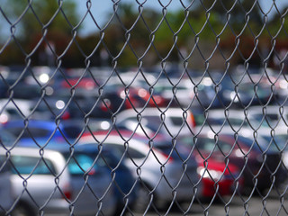 Wire mesh of a full outdoor car park or parking lot with blurry view of rows of cars parked inside.