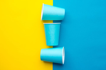 Blue paper disposable cups yellow and blue background. Cooking utensil. Cutlery sign. Top view. Minimalist Style. Copy, empty space for text